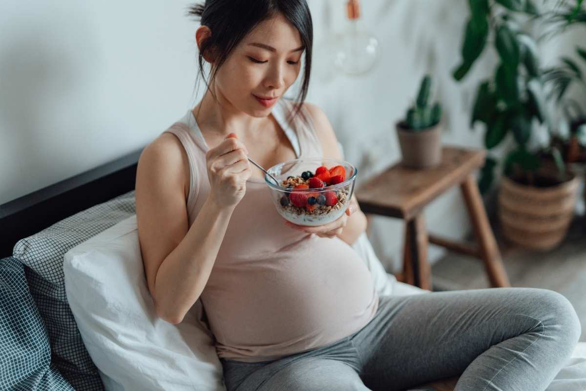 A young, happy pregnant woman eating healthy fruit and yoghurt